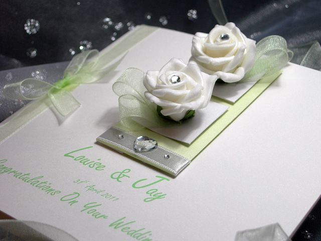 Chloe is a luxury handmade wedding card which is sure to WOW. This design uses pale green and white for an elegant look and feel. The card is made from white sparkle board which has a lovely subtle shimmer. The design features two white roses with diamant